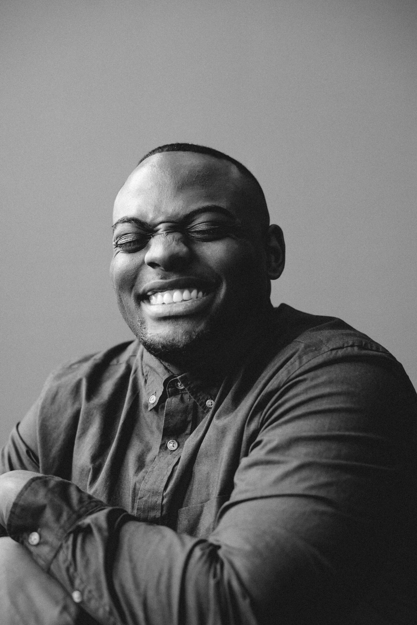A joyful black and white portrait of a smiling man in a button-up shirt.